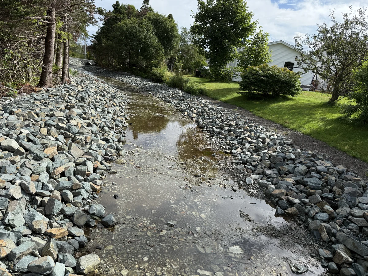 Rock-lined stormwater channel through a landscaped area in Torbay